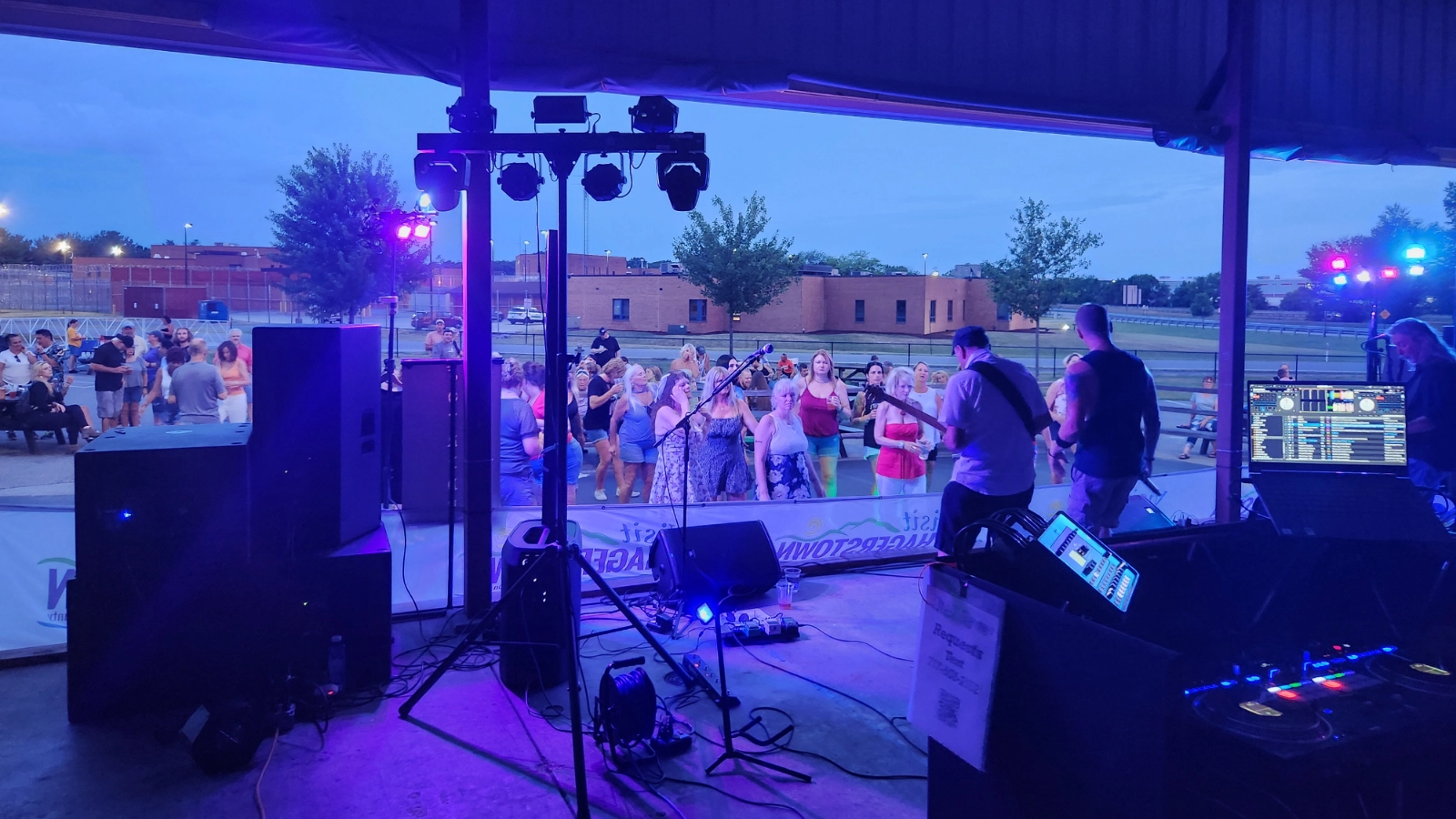 Guests enjoying live music at an open-air brewery event with DJ lighting and production equipment.