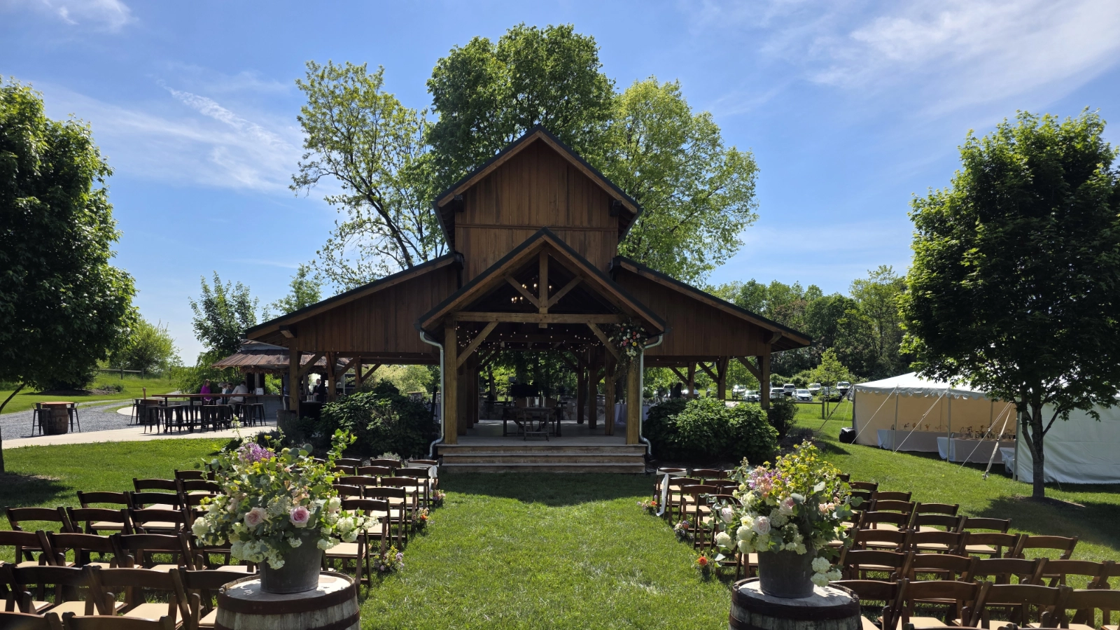 Outdoor wedding ceremony setup centered on a rustic pavilion with guest seating and floral aisle arrangements