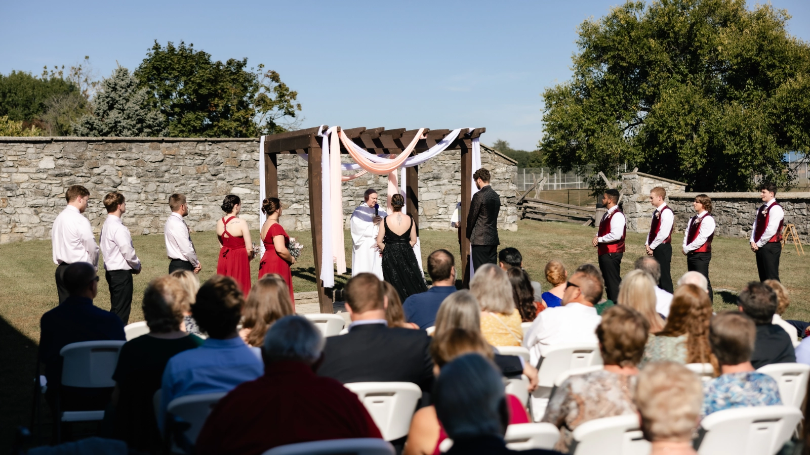 A couple standing with their wedding party during an outdoor ceremony as guests look on.