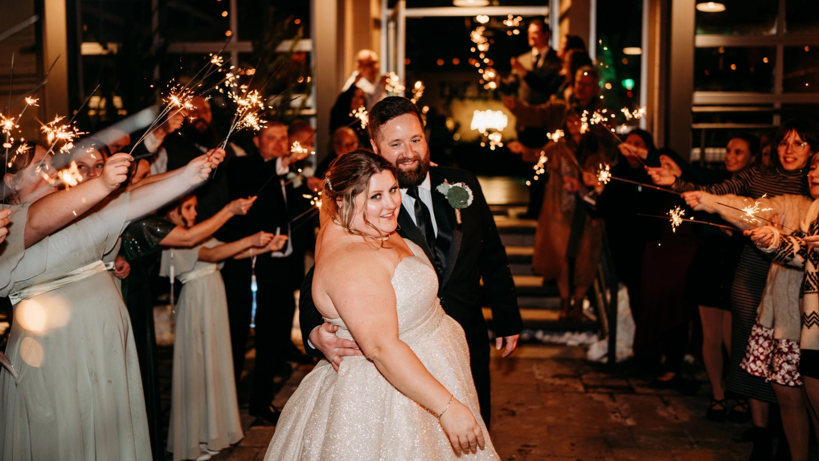 A newlywed couple walking together through a sparkler send-off surrounded by celebrating guests.