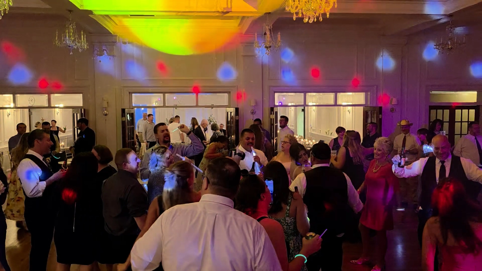 Wedding guests filling the dance floor under colorful DJ lighting in an elegant reception venue.